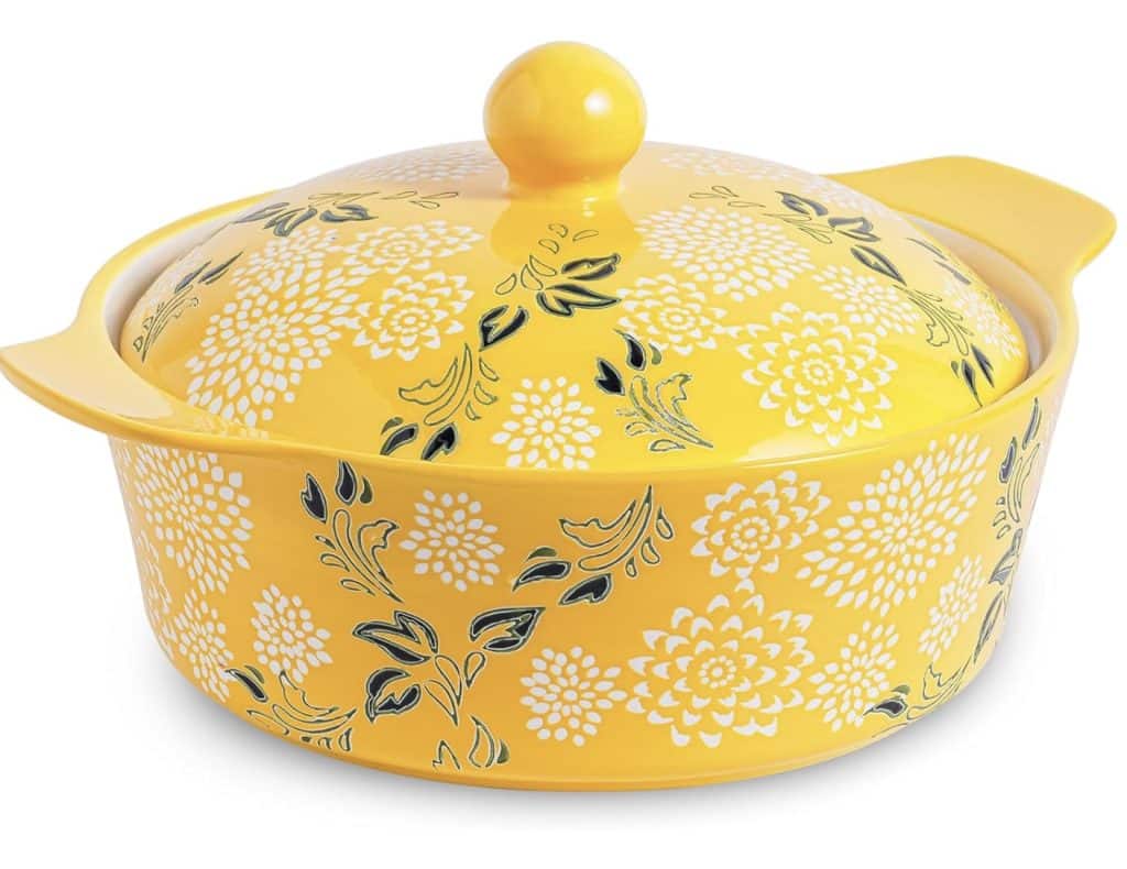 A round yellow ceramic casserole dish with a lid, decorated with white floral patterns and dark green leaves, is perfect for serving instant pot mashed potatoes, and features two convenient side handles.